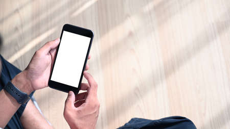 Close up view of young man hands holding mobile phone with blank screen while sitting on wooden floor.の写真素材