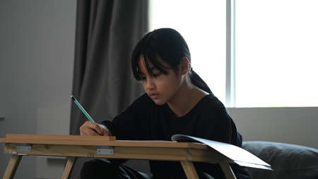 Smiling schoolgirl studying online lesson with digital tablet at home. Online education concept.の写真素材