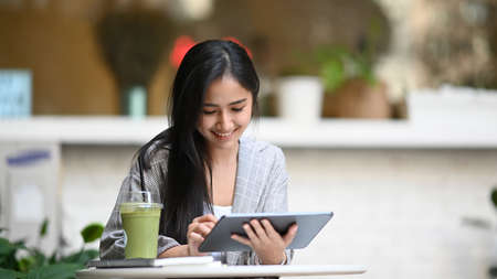 Smiling young businesswoman working with digital tablet and sitting at cafe with healthy vegetable drink.の写真素材