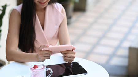 Cropped shot of young female relaxing at outdoor cafe and using smart phone.の写真素材