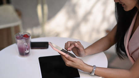 Cropped shot of young female relaxing at outdoor cafe and using smart phone.