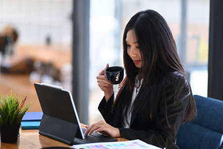 Portrait of attractive businesswoman scrolling through online information on digital tablet at modern office.の写真素材
