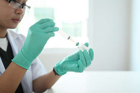 Young woman doctor or scientist holding injection syringe and vaccine.