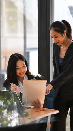 Two businesswoman colleagues sharing ideas about new corporate strategy at modern office.