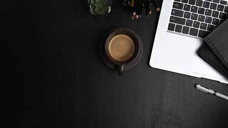 Overhead shot of contemporary workspace with laptop computer, coffee cup, notebook and copy space on black table.の写真素材