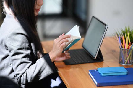 Businesswoman holding digital tablet and stylus pen while standing near window in office.の写真素材