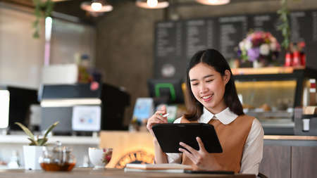 Happy young woman talking on mobile phone and looking at camera while siting in modern coffee shop.の写真素材