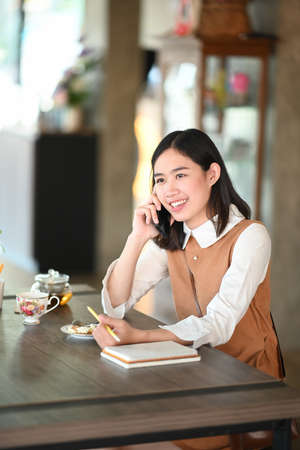 Portrait of young woman holding digital tablet and smiling to camera while sitting in coffee shop.の写真素材