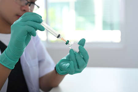 Close up view of doctor hand wears medical glove holding syringe and vaccine bottle.