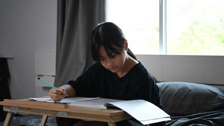 Happy young school girl studying online with computer tablet at home.の写真素材