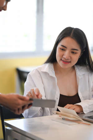 Young asian woman waitress holding digital tablet receiving orders from customers.