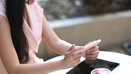 Cropped shot of businesswoman holding horizontal mobile phone while sitting at outdoor.の写真素材