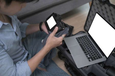 Photographer sitting on wooden floor and putting camera accessories in special bag.