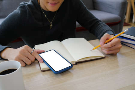 Young male university student doing some homework and using smart phone.の写真素材