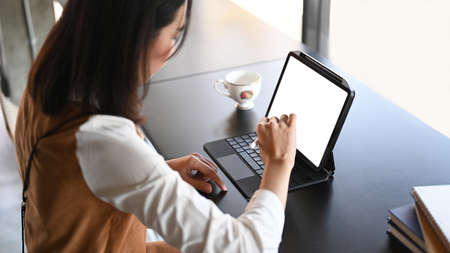 Side view of female designer holding stylus pen writing on digital tablet at coffee shop.