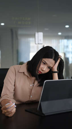 Young woman office worker holding her head and suffering stress working.の写真素材