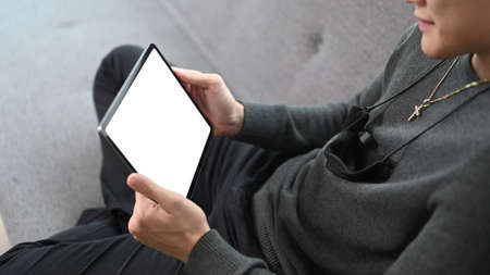 Close up view man holding horizontal digital tablet and sitting on couch at home.