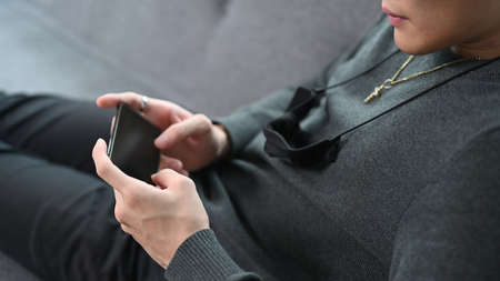 Close up view of young man holding mobile phone with blank screen while sitting in front of computer...