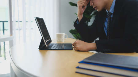 Confident businessman using smart phone and working with laptop computer at office desk.の写真素材