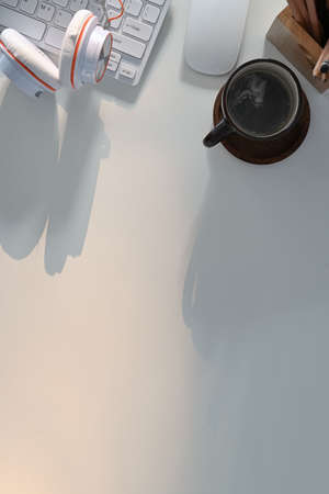 Top view of modern workplace with headphone, coffee cup, keyboard, glasses and copy space on white table.の写真素材