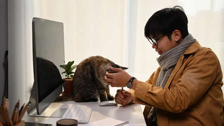 Cropped shot of young man reading news on digital tablet while sitting with his cat at home office.の写真素材
