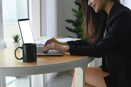 Side view of smiling young woman accountant working on laptop computer at office desk.の写真素材