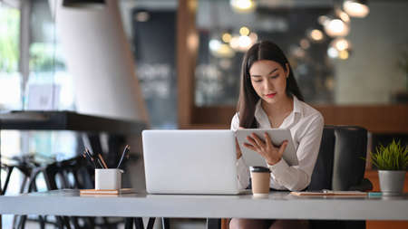 Businesswoman working with laptop computer and looking information on digital tablet.の写真素材