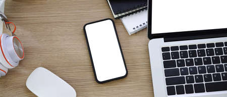 Horizontal photo of mock up smart phone and laptop computer with blank screen on wooden table.