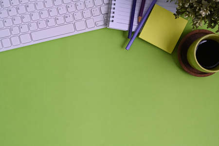 Top view of stylish workplace with keyboard, coffee cup, notebook and copy space on green background.の写真素材