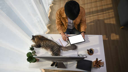 Cropped shot of young man using smart phone and working with computer laptop at modern home office.の写真素材