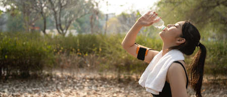 Portrait of sporty woman with white towel smiling to camera and standing in the public park.