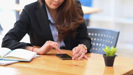 Cropped shot of businesswoman using smart phone on wooden office desk.の写真素材