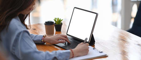 Cropped shot of businesswoman sitting at wooden office desk working on computer tablet and making...