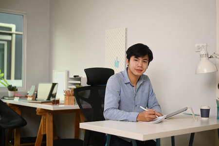 Cropped shot of businessman holding pen writing on empty notebook at office desk.の写真素材