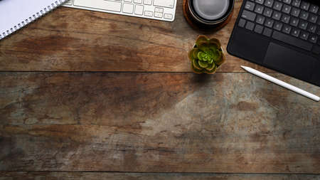 Top view of modern workplace with digital tablet, keyboard, plant and notebook on white office desk.