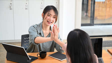 Two young female colleagues giving high five to celebrating achievement in office.の写真素材