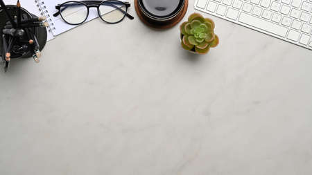 Overhead shot of white office desk with smart phone, notebook, coffee cup, glasses and keyboard.の写真素材