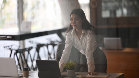 Confident businesswoman sin black suit sitting with arms crossed in modern office.の写真素材