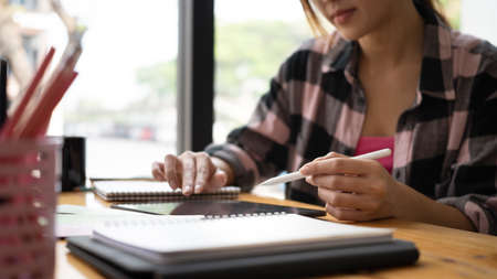 Portrait of young designer sitting near window in coffee shop with her computer table and smiling to camera.の写真素材