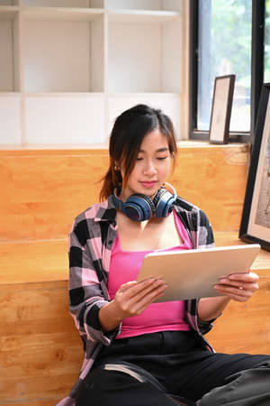 Portrait of thoughtful young woman sitting in coffee shop with her computer tablet and looking out of window.の写真素材