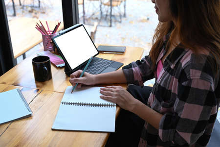 Portrait of thoughtful young woman sitting in coffee shop with her computer tablet and looking out...