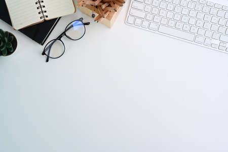 Top view of white office desk with keyboard, eyeglasses and notebook. Copy space for advertise text.