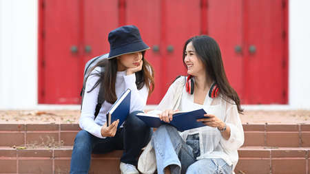Two college student reading interesting book and prepare for exam while standing together in campus.の写真素材