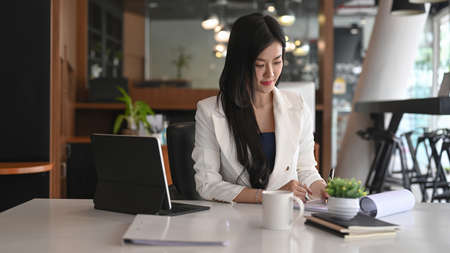 Confident female entrepreneur holding files and standing in modern office.の写真素材