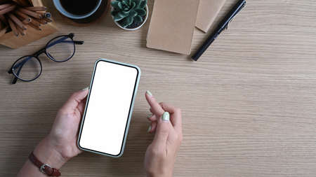 Hands of woman holding and typing on smart phone over her workplace.の写真素材