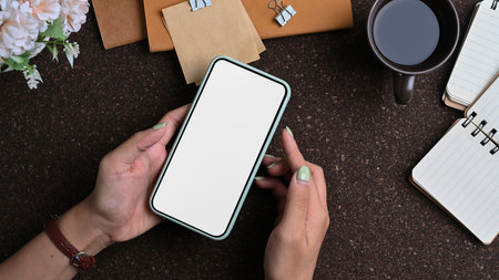 Overhead shot of businessman holding horizontal smart phone with blank screen at his workplace.