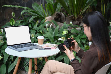 Young female freelancer sitting at outdoor cafe and checking photo on her camera.