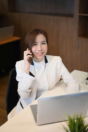 Portrait of successful businesswoman talking on mobile phone and working with computer laptop at her...
