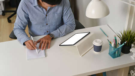 Young man freelacer working with digital table and making note on notebook at home office.