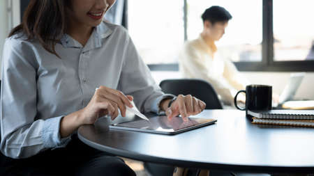 Cropped shot of happy businesswoman smiling and working o digital tablet with her colleague sitting in background.の写真素材